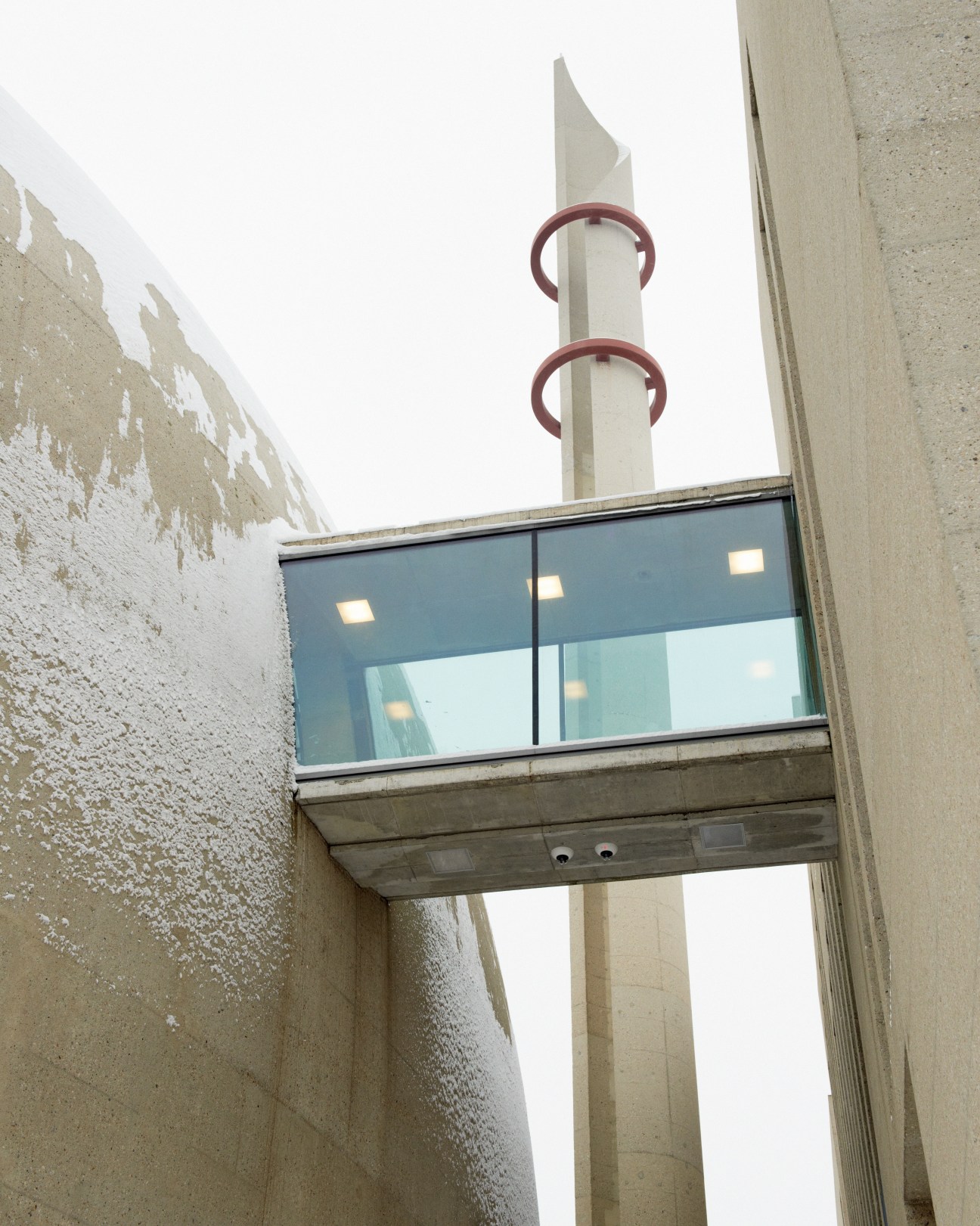 Concrete covered walkway with glass panels and a minaret with red rings at the Central Mosque in Köln.