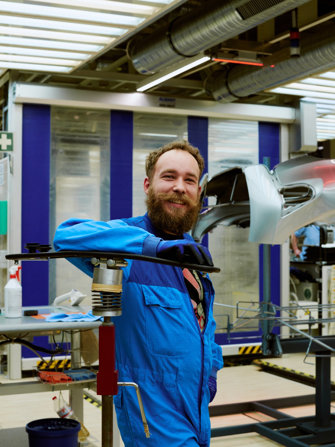 Male worker in blue uniform inspects painted car part under bright light in BMW factory.