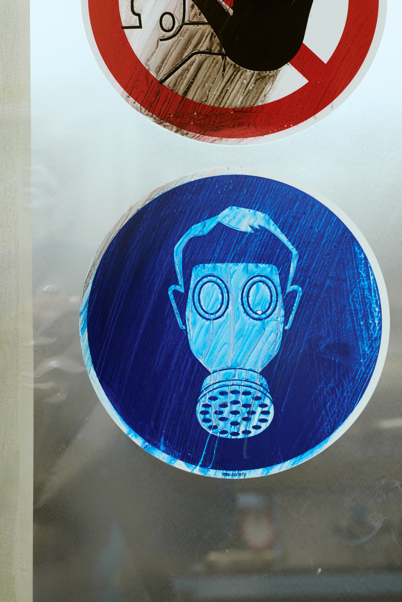Circular hazard warning signs with red and blue backgrounds depicting a gas mask symbol on a wall.