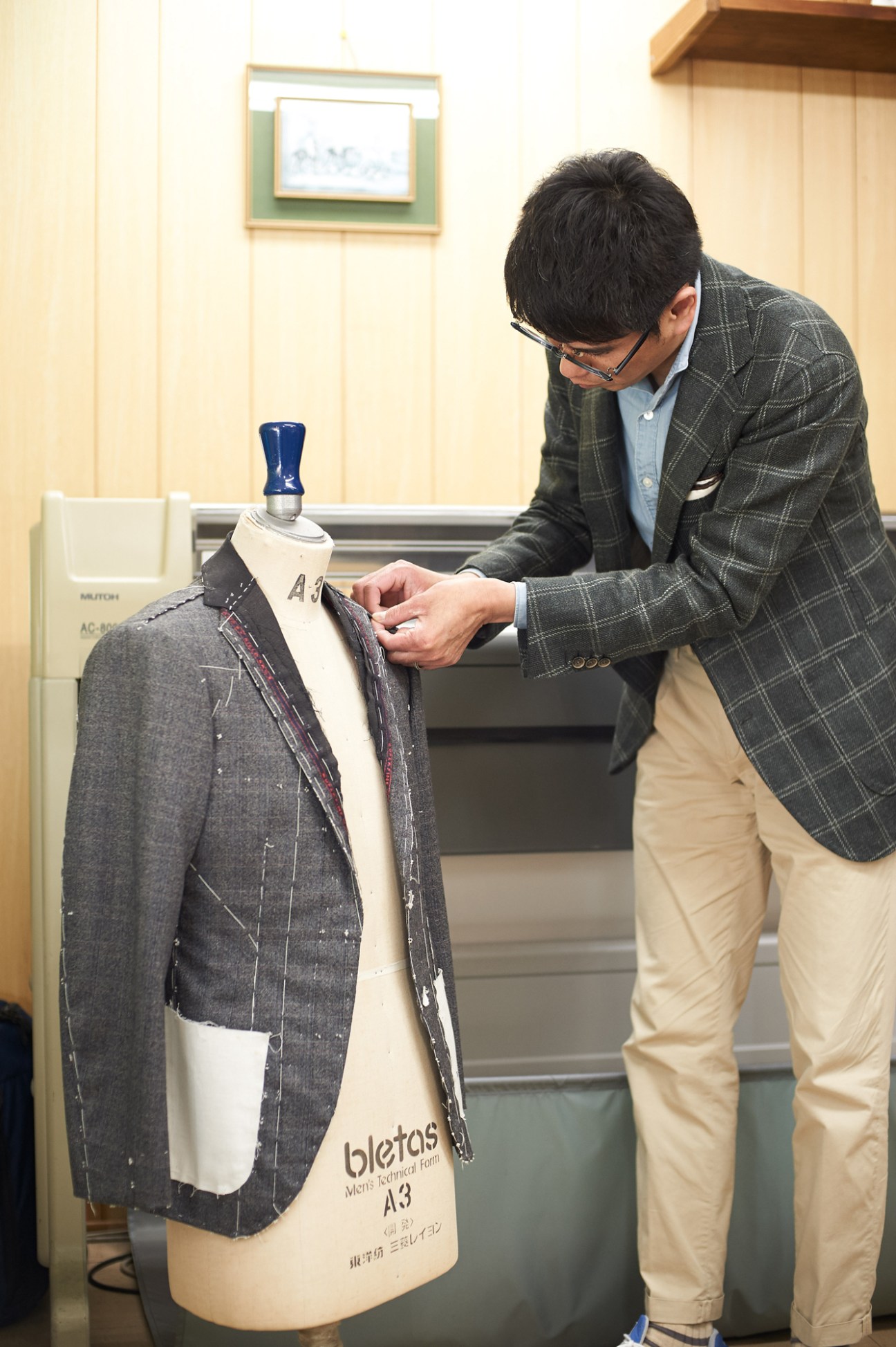 Tailor adjusting pinstripes on a charcoal suit jacket displayed on a dress form.