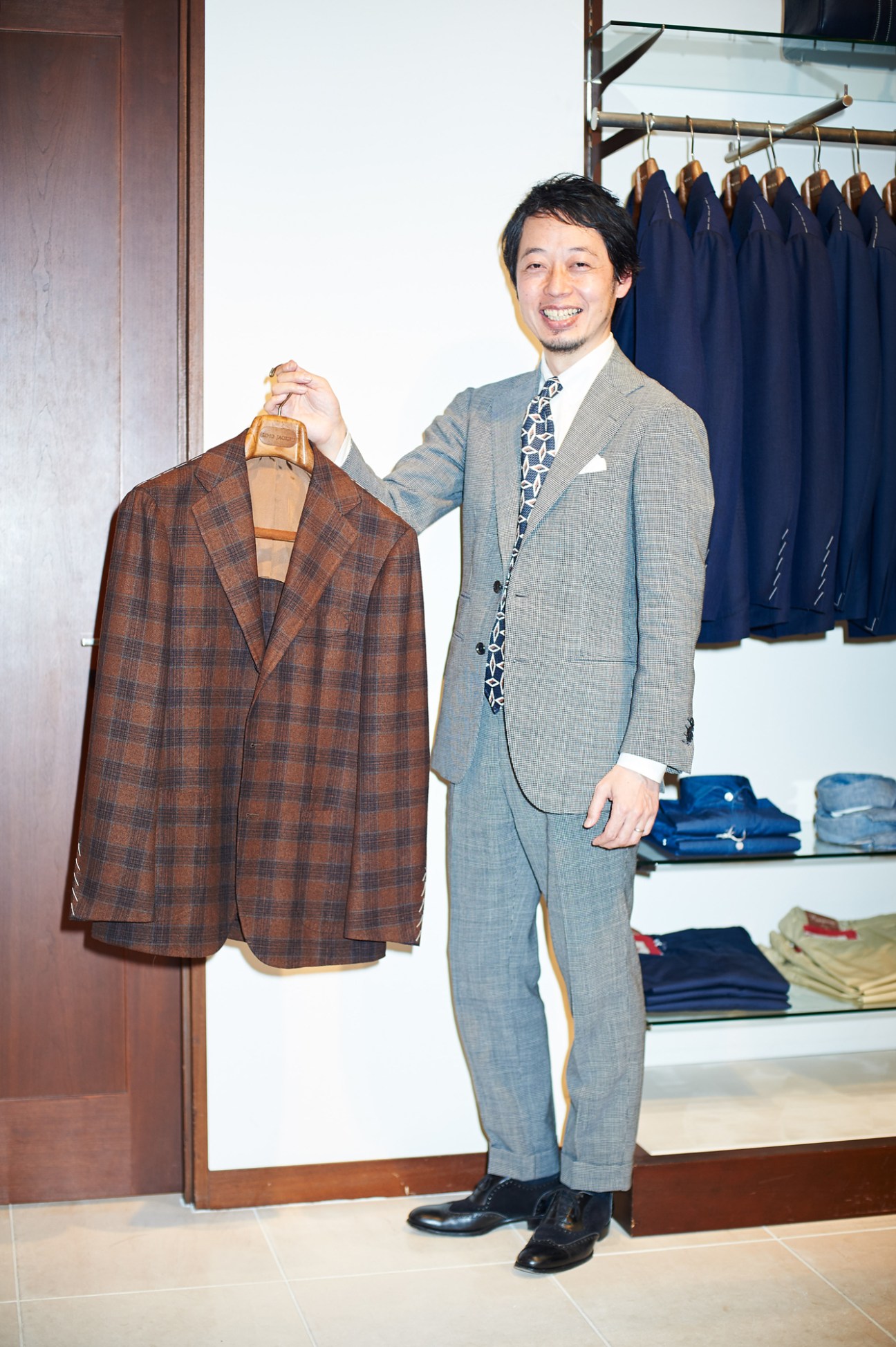 Takeshi Okuno holds a brown plaid blazer on a hanger in his suit showroom.