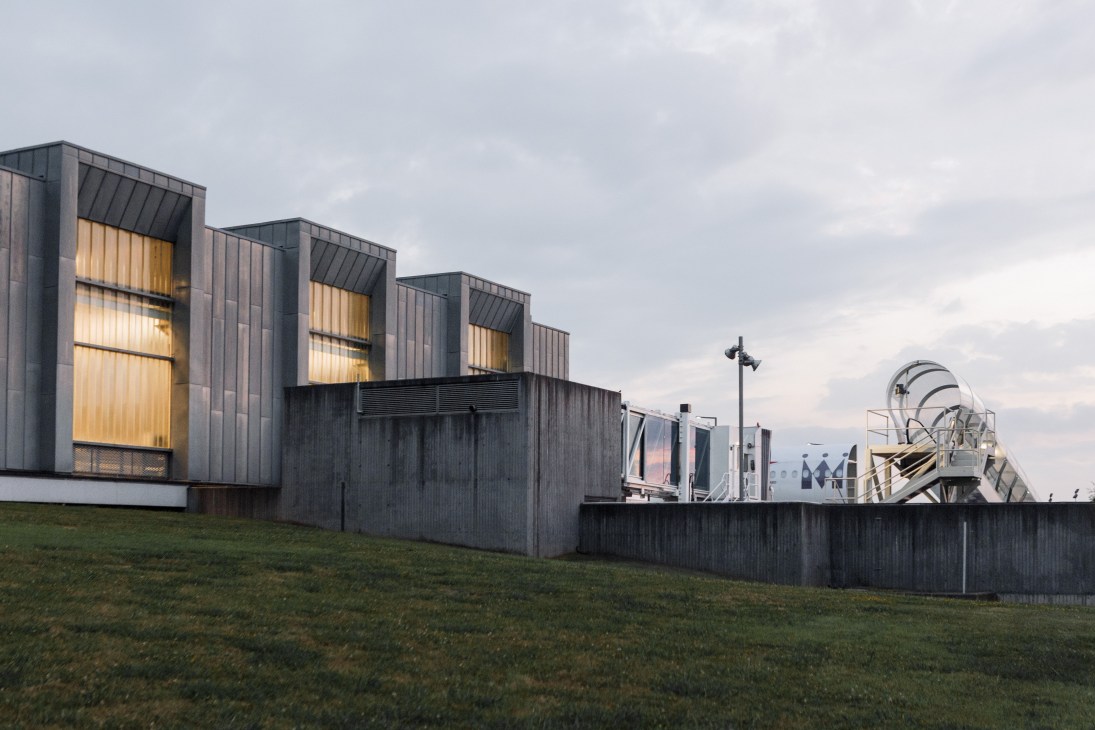 Modern black corrugated metal building with large golden-lit windows set in a grassy landscape.