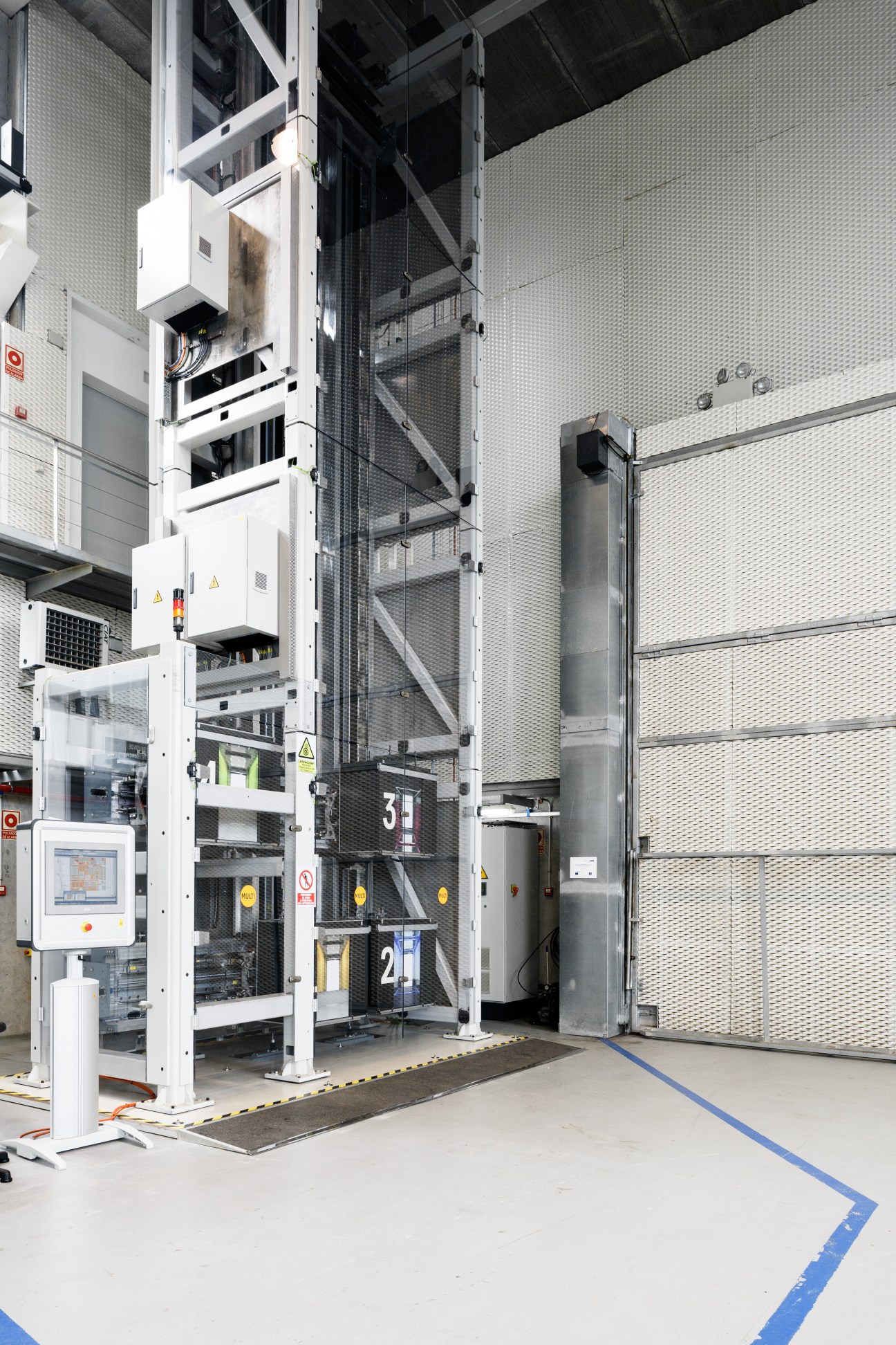 Industrial elevator testing equipment with white frame and black mesh safety cage in a research facility.