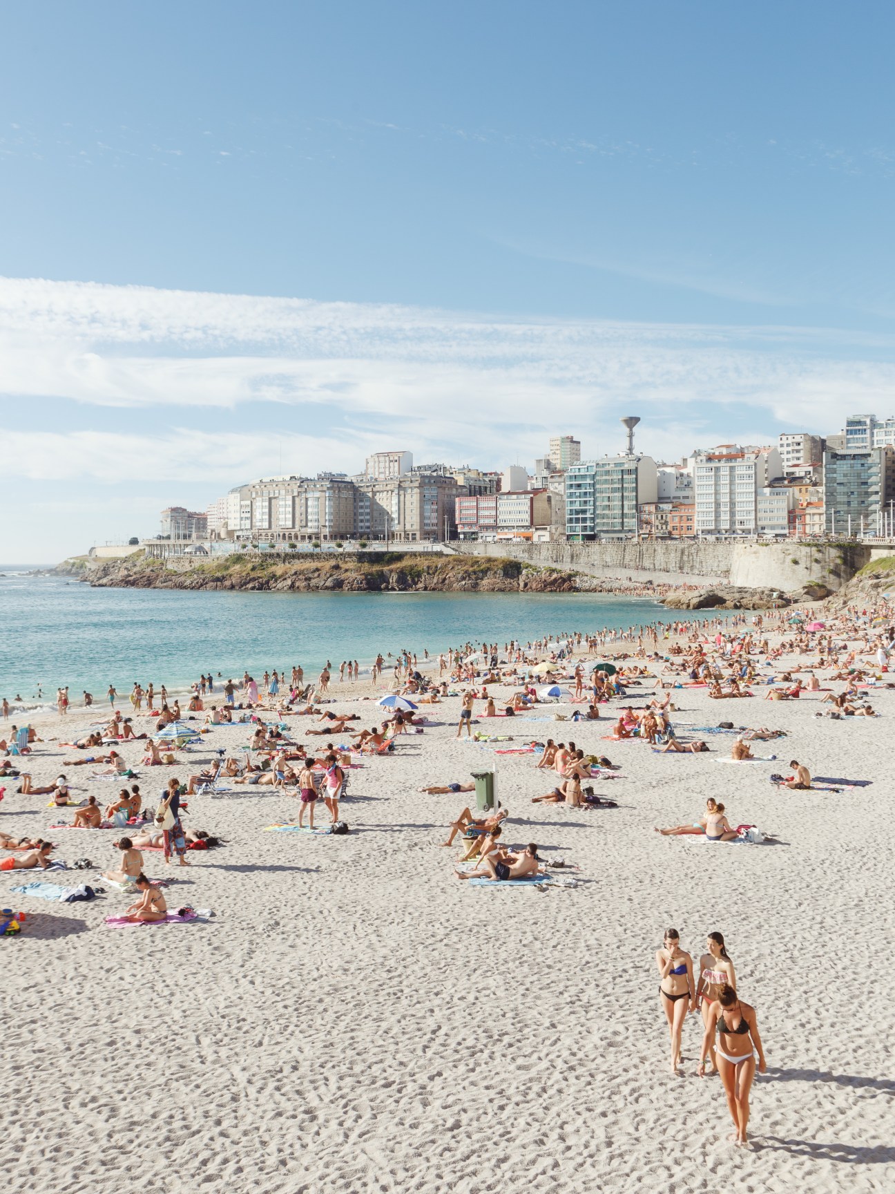 Crowded beach with turquoise water and seaside buildings in A Coruña, Spain.