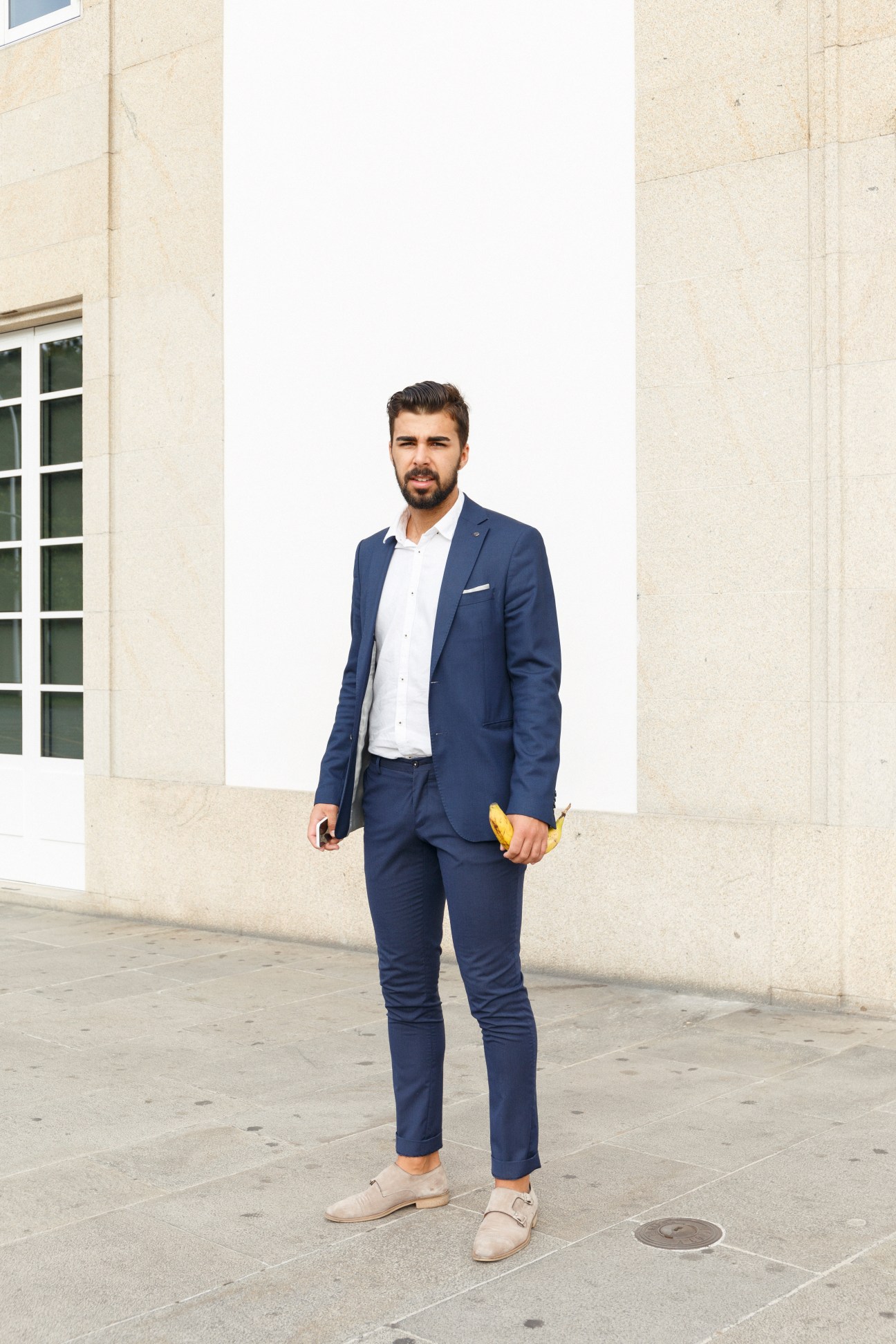 Man in navy blazer and white shirt standing against modern stone building