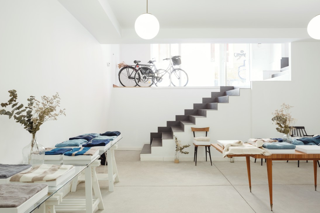 Modern showroom interior with white walls, floating staircase, bicycles on upper level, and Knitbrary textile displays.