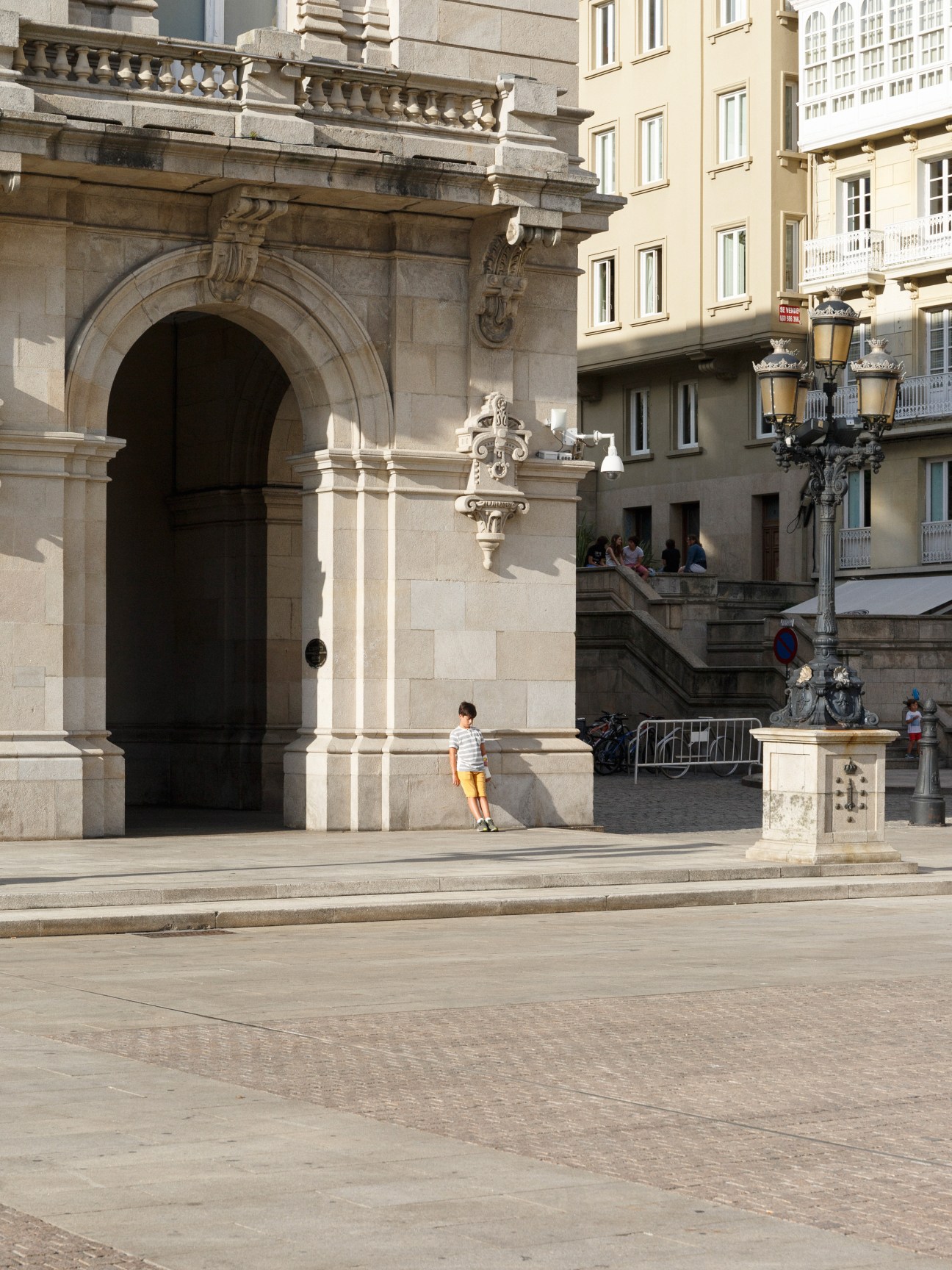 Child in striped shirt standing alone in Plaza Mayor archway, A Coruña.