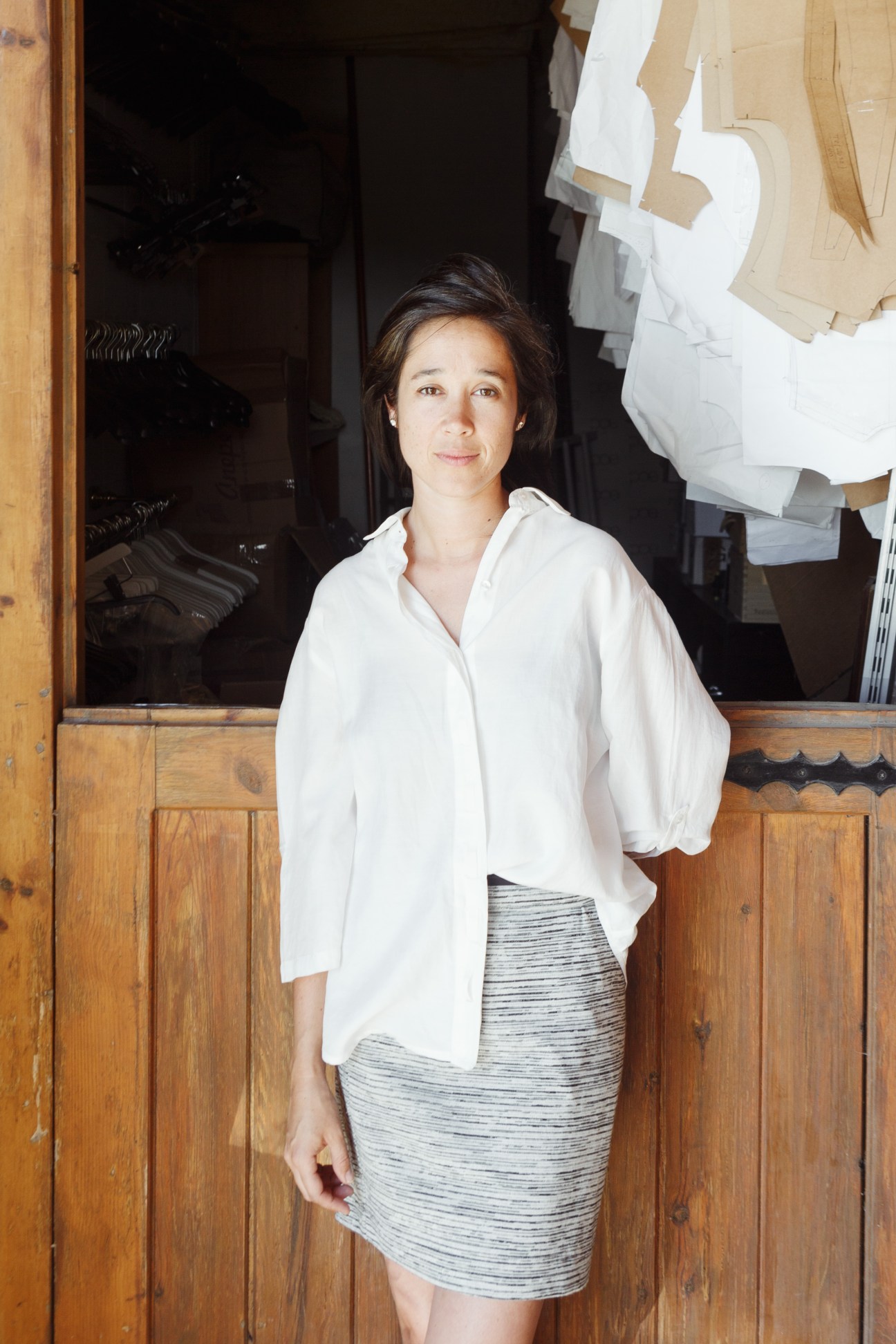 Leticia Garnelo, founder of women's fashion brand Poe, standing in a shop doorway wearing a white shirt and gray skirt.