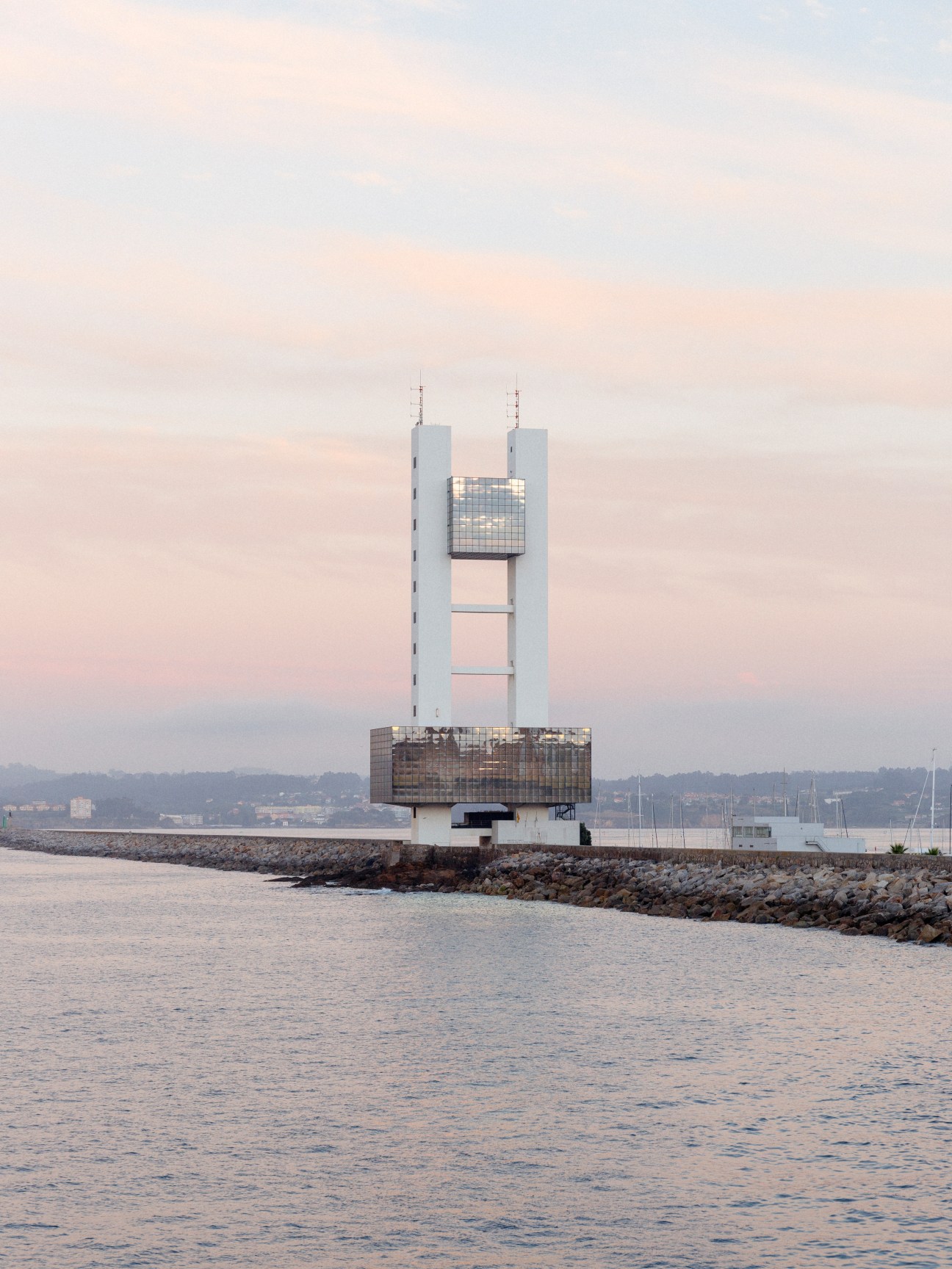 Modern lighthouse structure with twin white towers and dark mid-section at A Coruña's port entrance.
