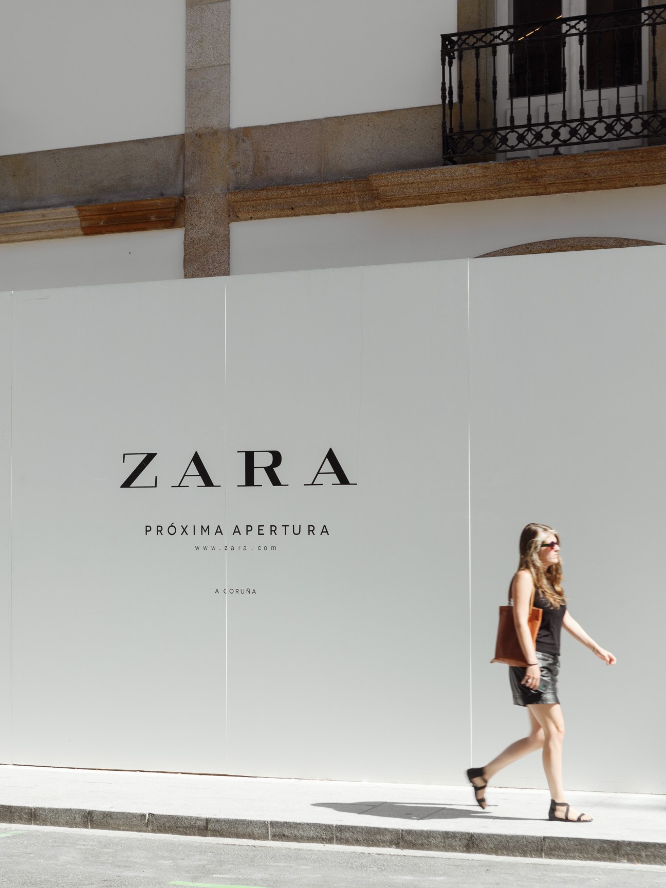 Woman walking past a Zara storefront advertising its next opening in A Coruña