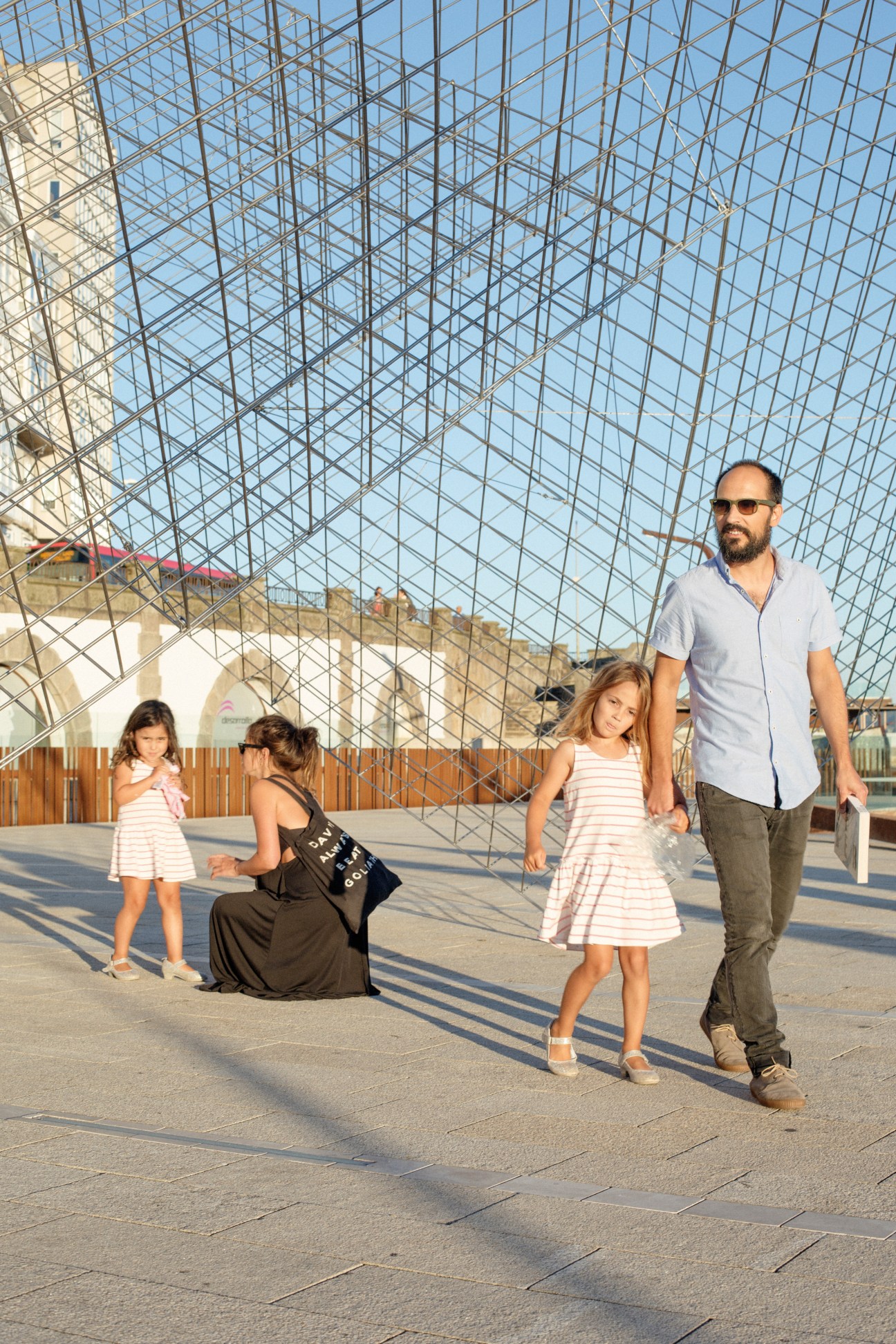 Family walking on a waterfront promenade under a modern glass and steel structure.