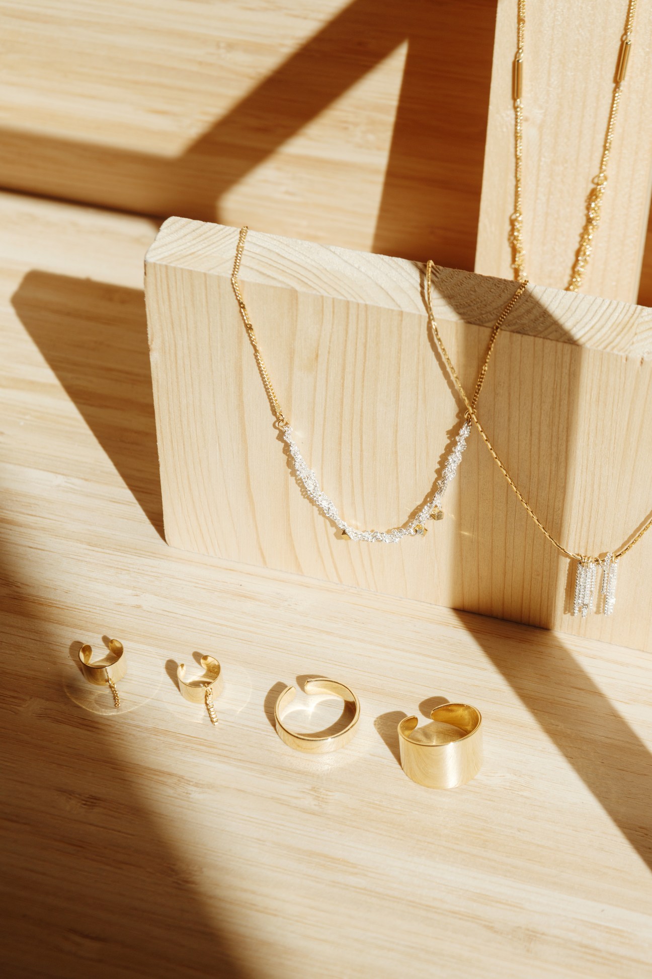 Gold and diamond jewelry pieces displayed on wooden blocks in natural light.