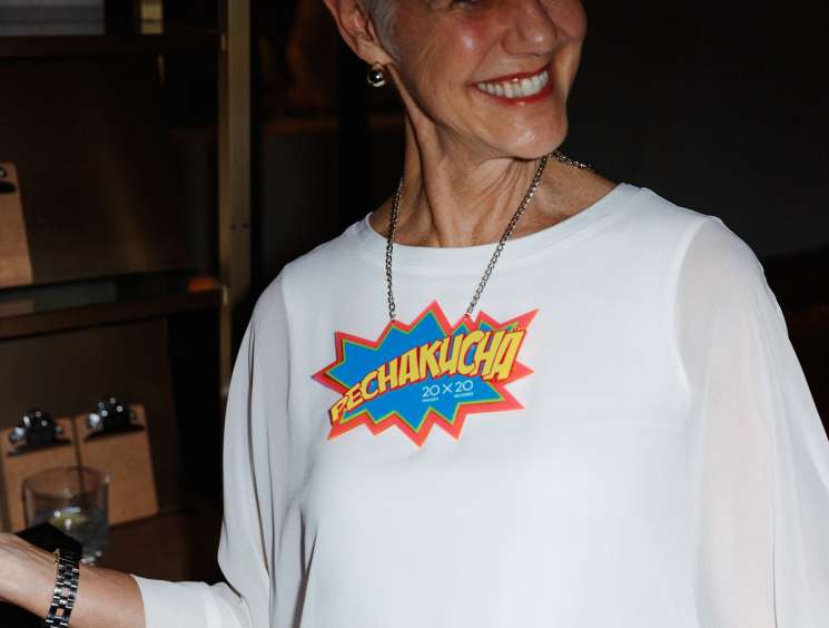 Woman in white PechaKucha sweatshirt smiling at event venue