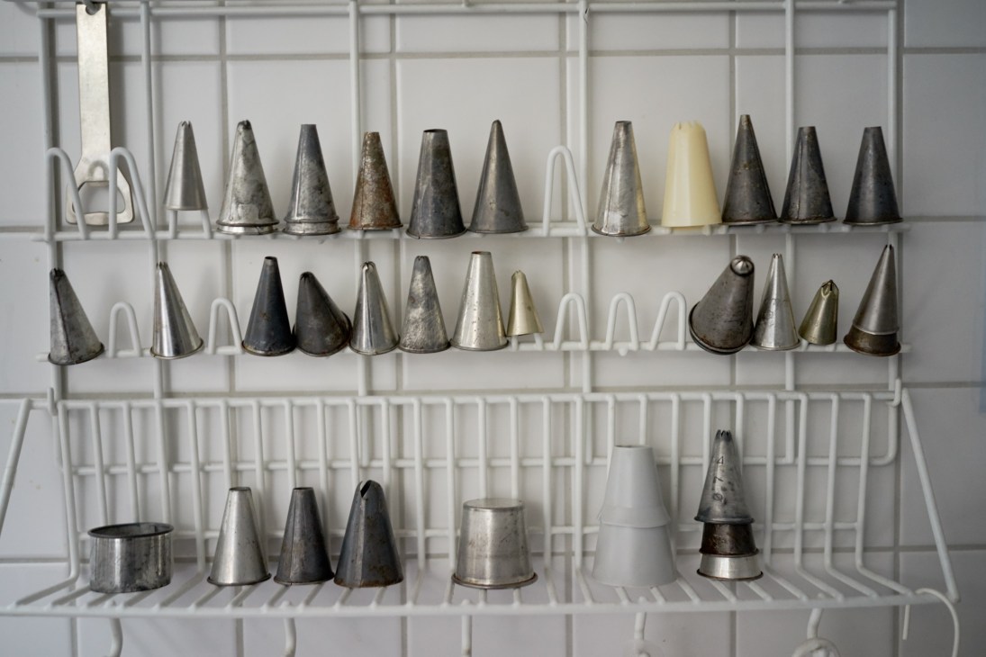 Metal piping nozzles and attachments displayed on a white organizer rack.