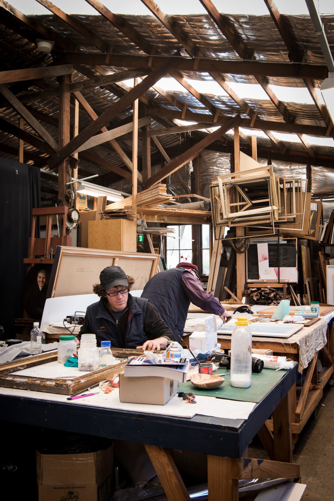 Painter Robert Dujin and sculptor Stephen Coburn working in their shared studio at Headland Park with wooden beams overhead.