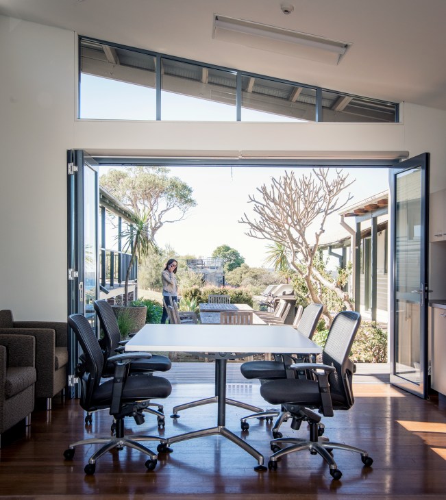 Modern conference room with glass doors opening to a terrace overlooking harbour landscape with trees.