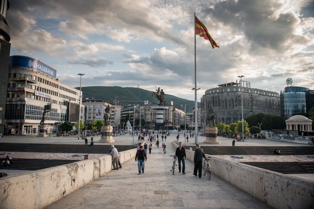 Macedonia Square in Skopje with equestrian statue, Macedonian flag, and surrounding neo-classical buildings.
