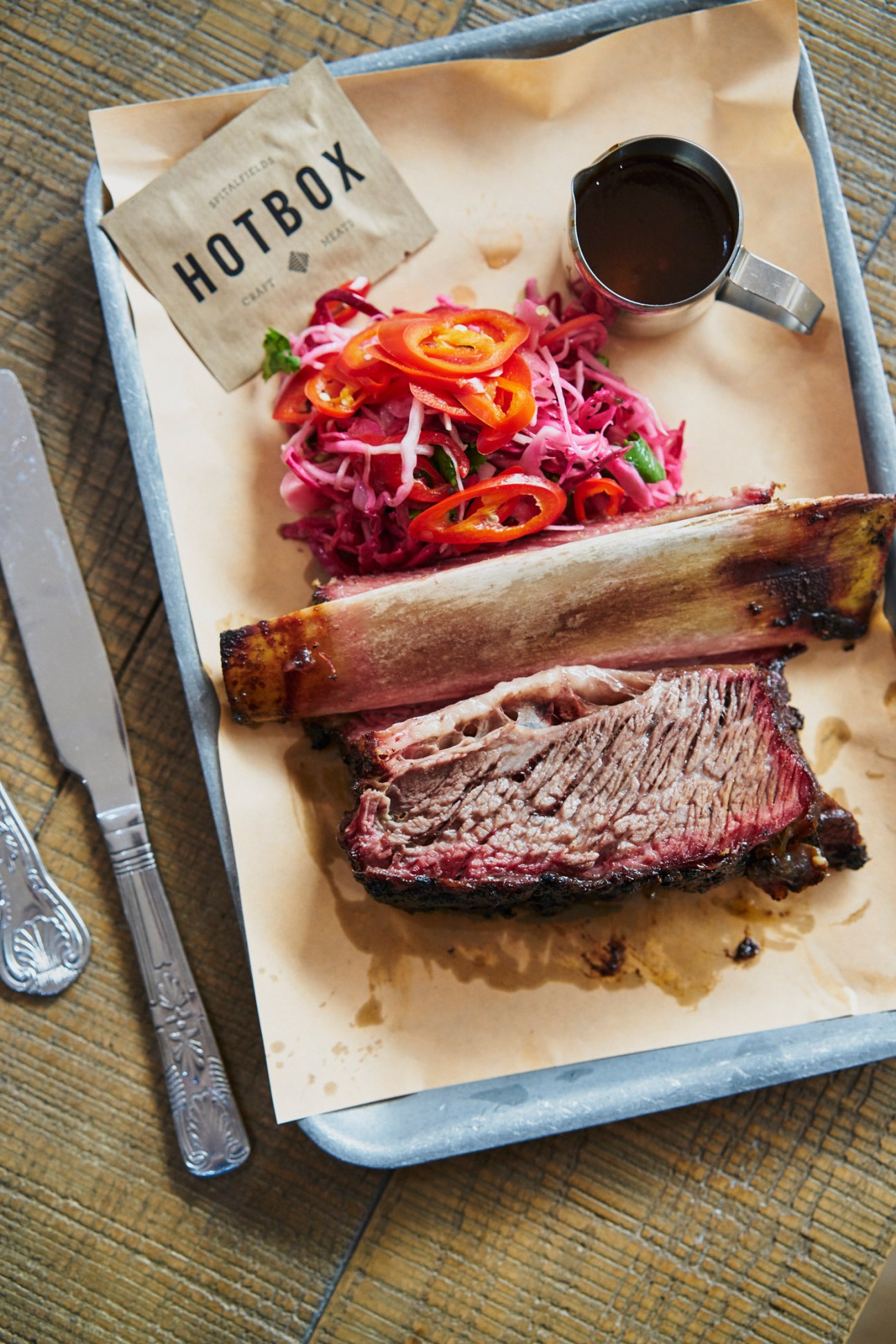 Smoked meat cuts on parchment paper with pickled vegetables and Hot Box branding on wooden table.