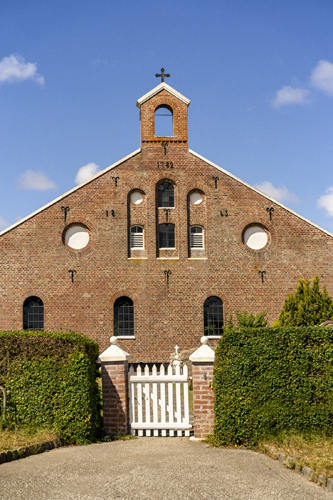 Brick church building with cross on bell tower and white gate entrance in Sønderho