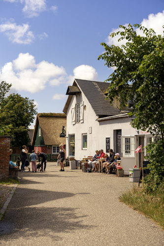 White traditional Danish house with outdoor seating area where people gather under blue sky with clouds