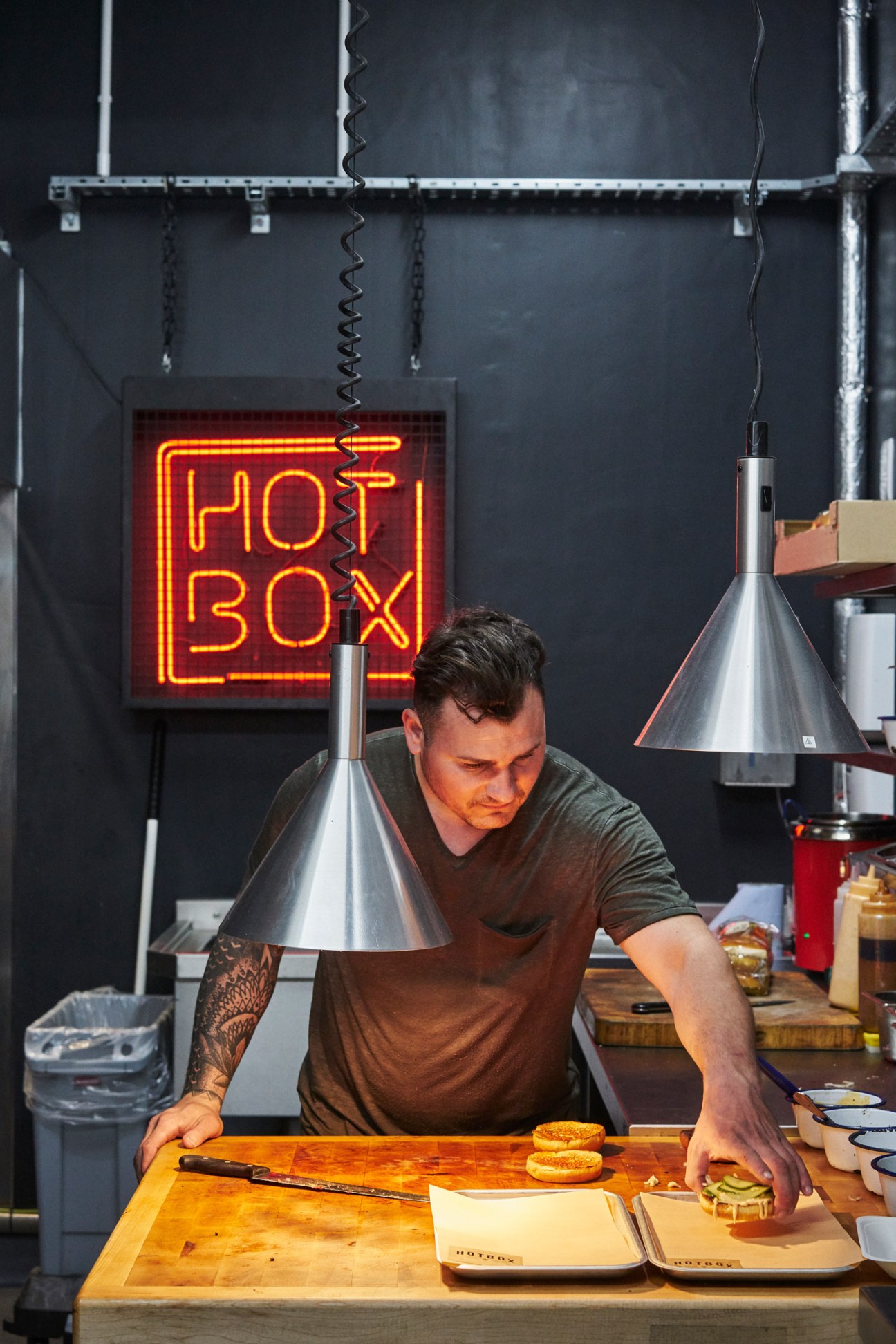 Chef preparing food at Hot Box counter under neon sign and heat lamps.