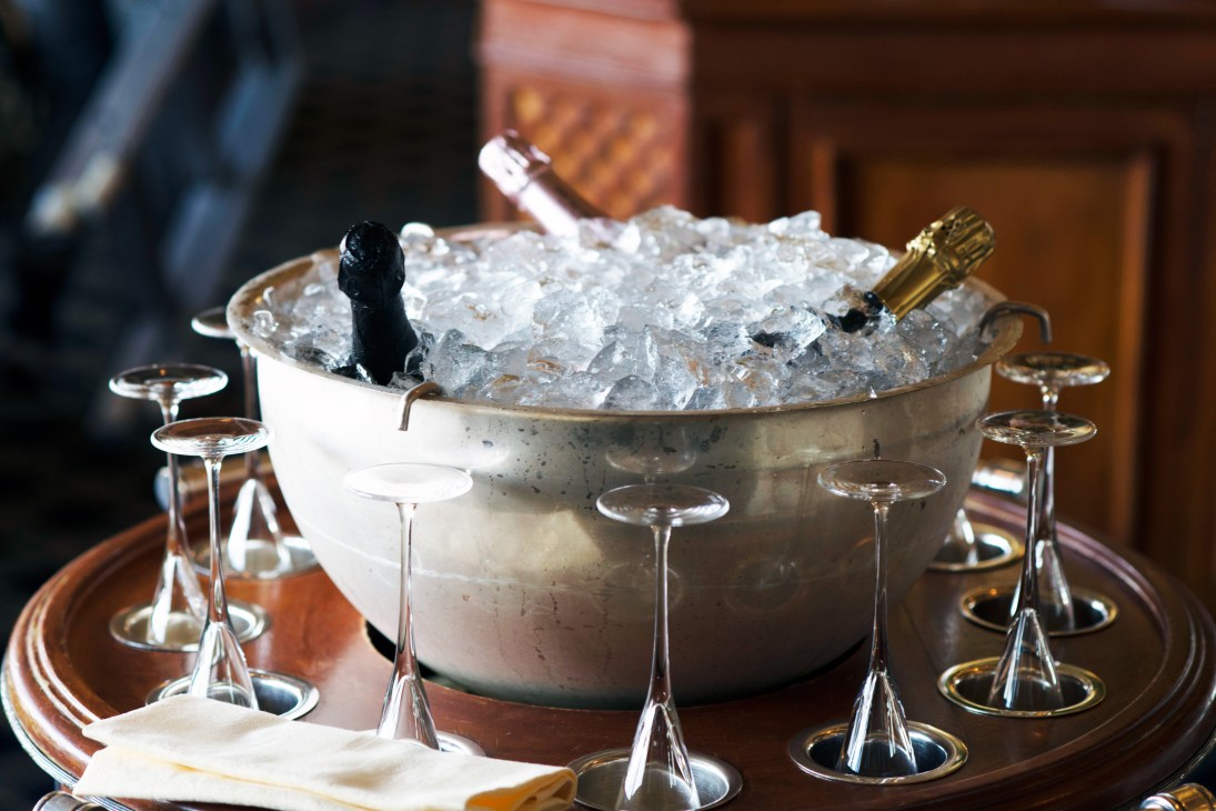 Champagne bottle chilling in ice bucket surrounded by empty champagne flutes at an elegant dining table.