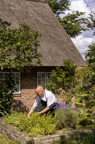 Jakob Sullestad working in a garden with traditional thatched-roof building in background