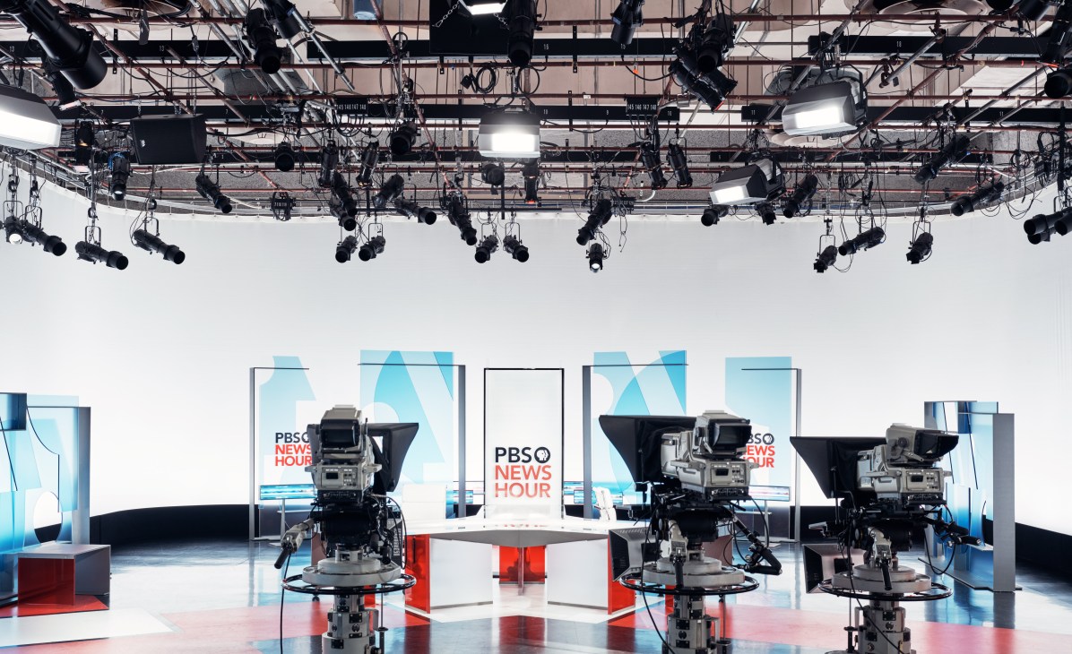 PBS Newshour studio with suspended cameras and lighting rigs above an empty anchor desk.