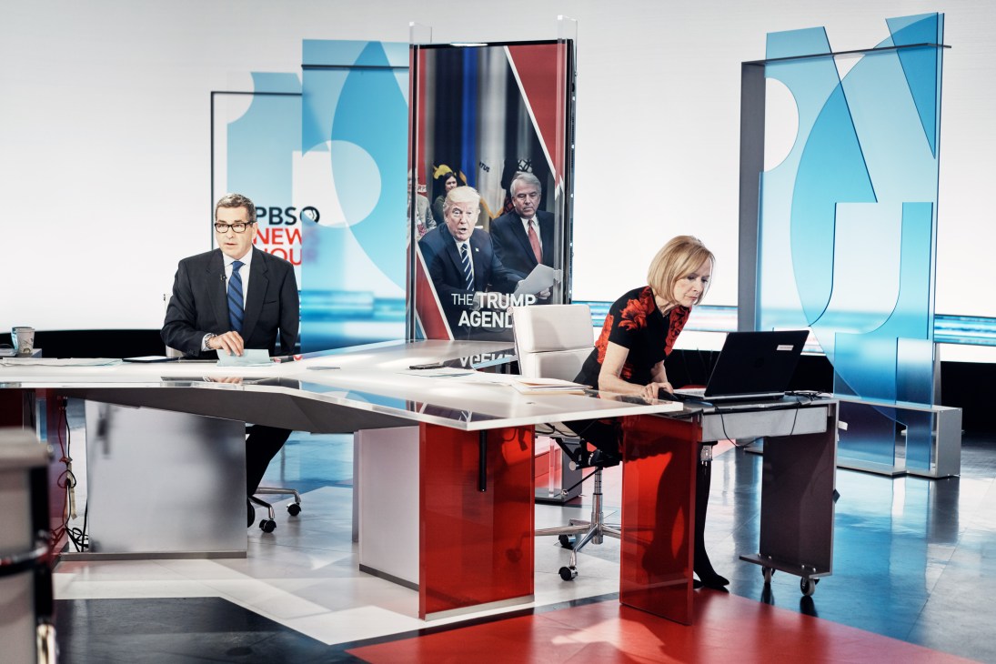PBS Newshour anchors Miles O'Brien and Judy Woodruff at desks in the studio during a pre-recorded segment.