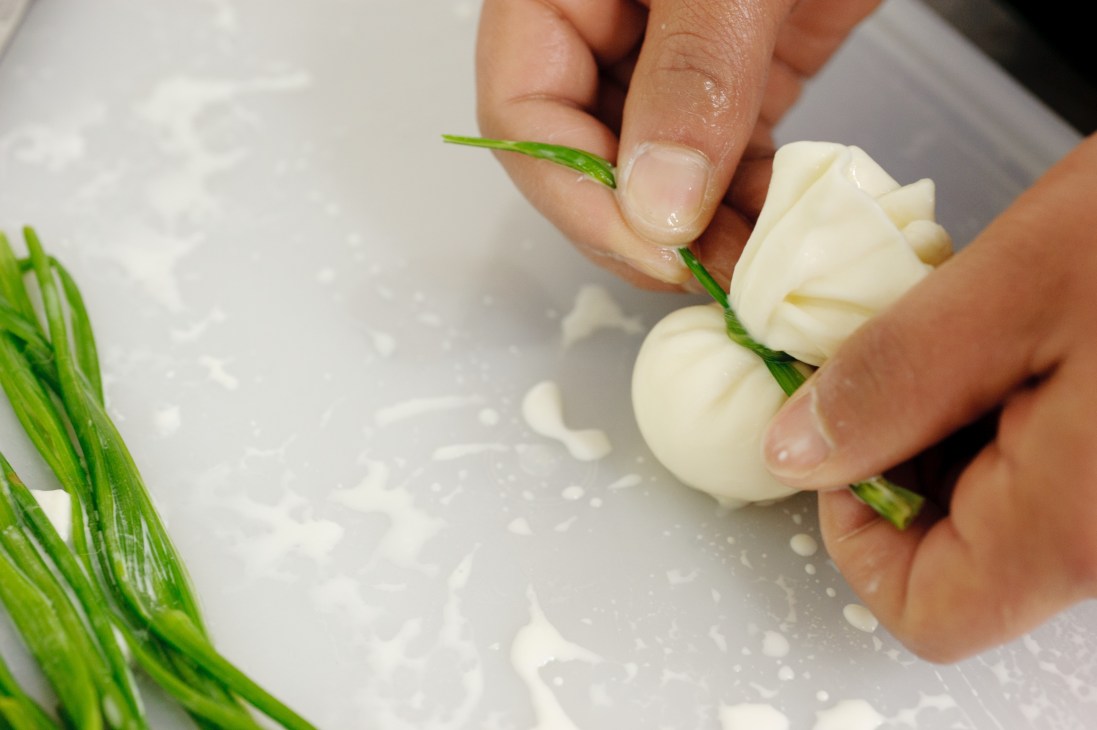 Hands preparing fresh mozzarella with green Chinese leek on a white surface at Solo Latte.