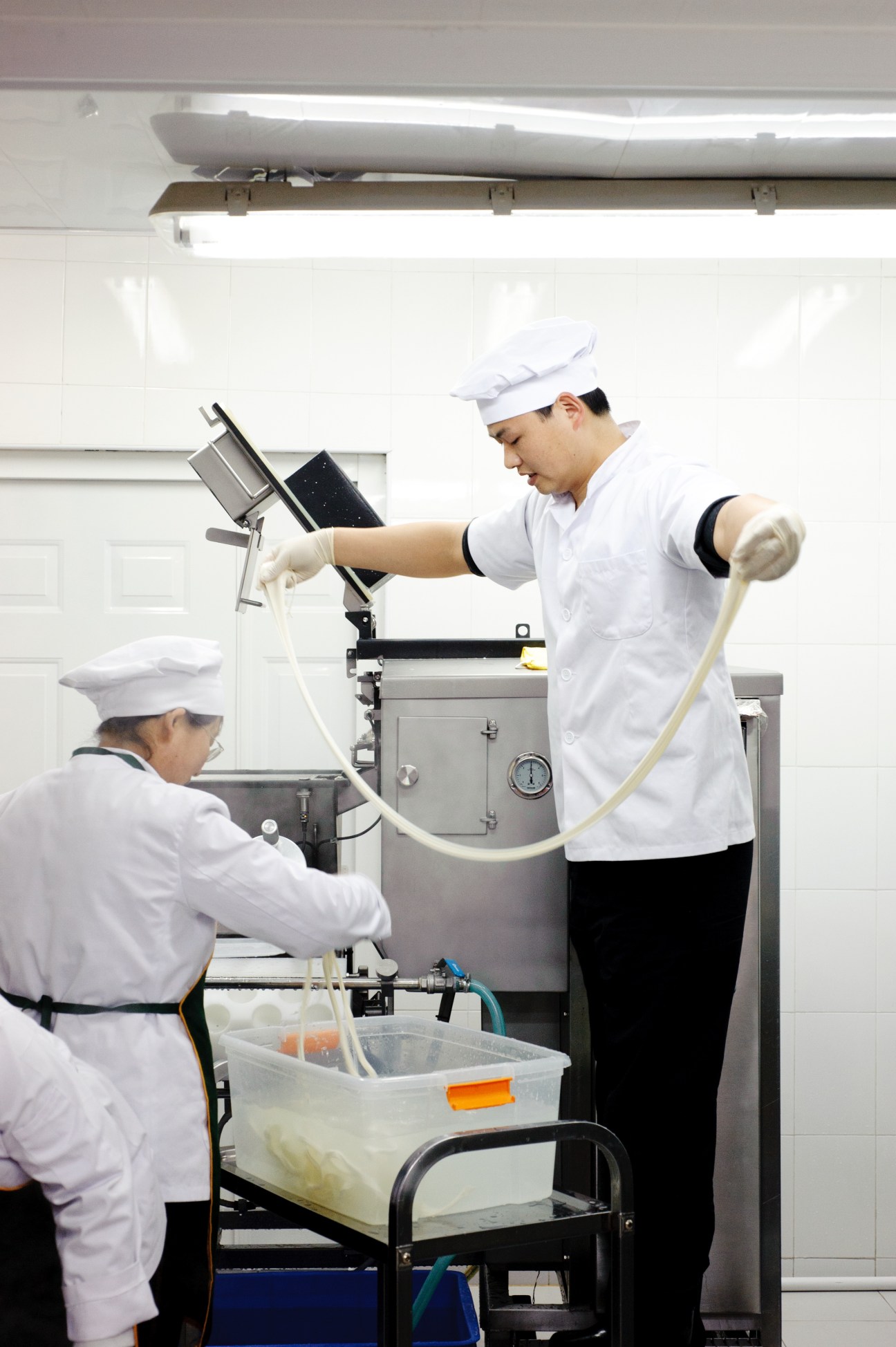 Two cheesemakers in white uniforms and chef hats work together at mozzarella production equipment at Solo Latte.