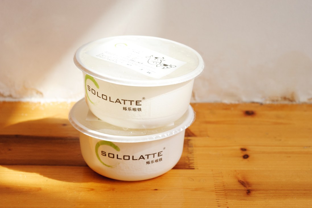 Two stacked Solo Latte mozzarella containers on a wooden surface in sunlight.