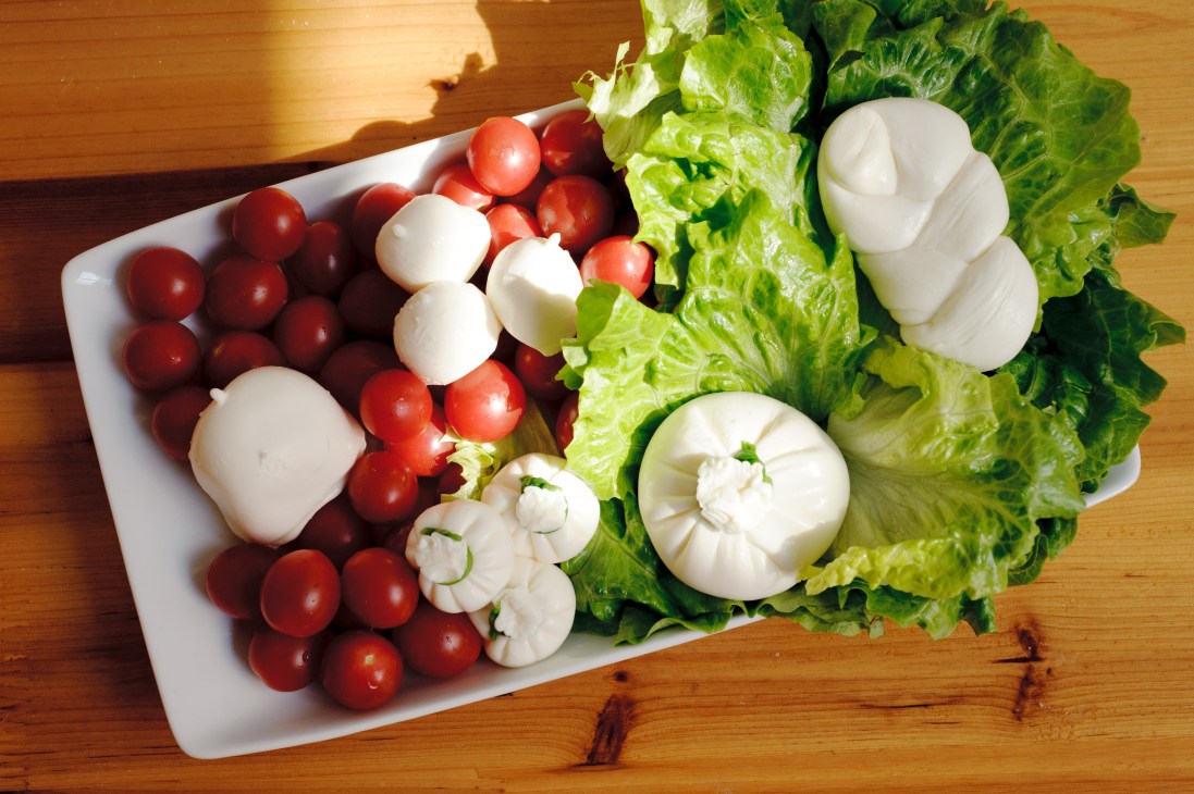 Fresh mozzarella balls with cherry tomatoes and lettuce on a white plate.