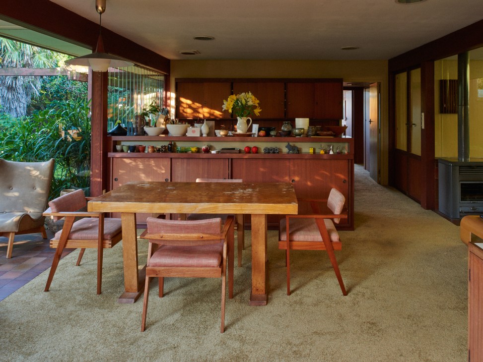 Modernist dining area with wooden table, mid-century chairs, and original kitchen cupboards with display shelving.