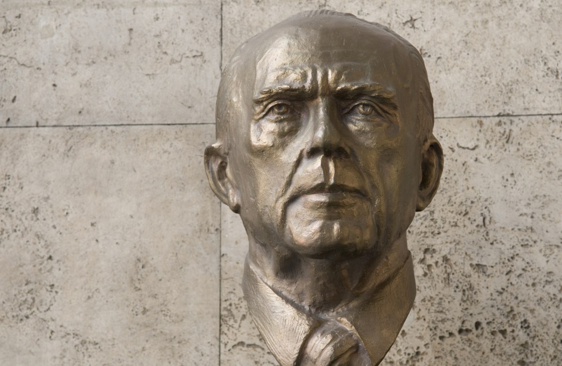 Bronze bust sculpture of architect Hayati Tabanlioglu against a concrete wall.