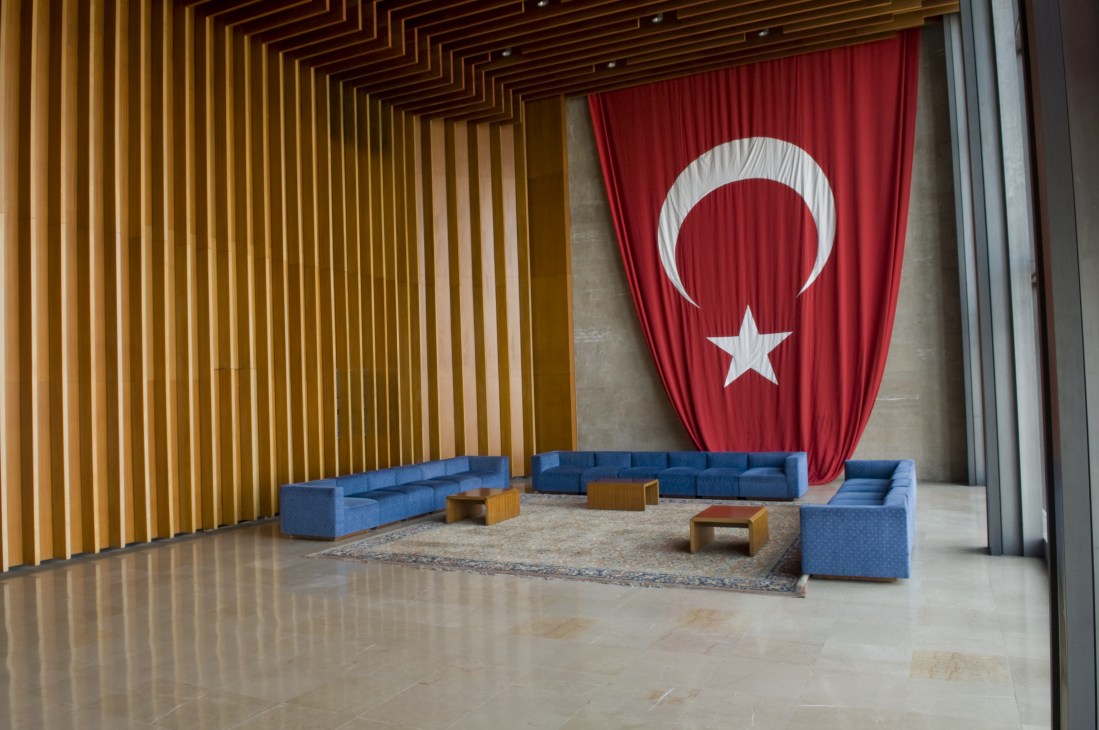 Turkish flag with crescent and star hangs in modernist foyer with blue seating and golden vertical slats.