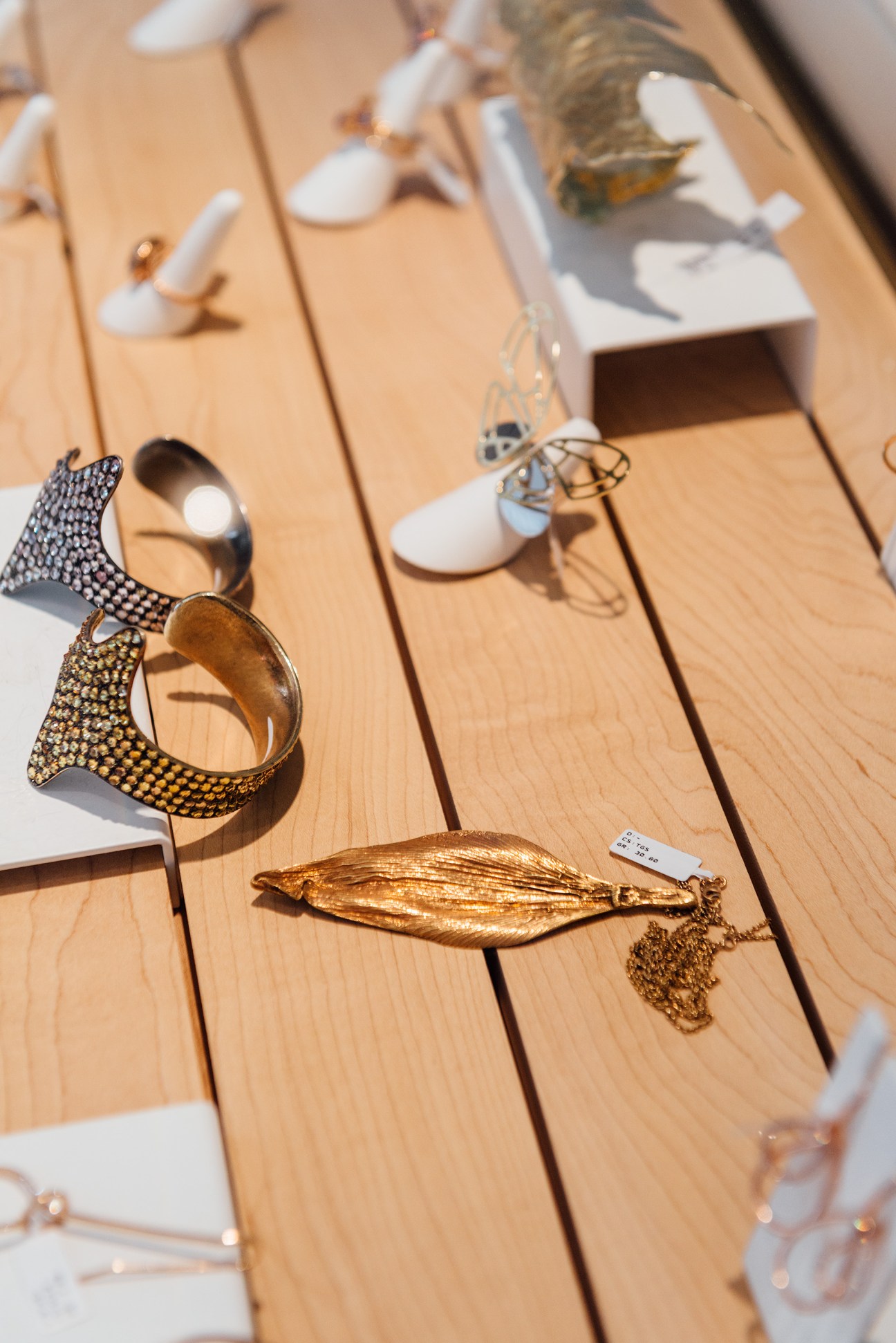Gold and silver jewellery pieces displayed on a light wooden table with white stands.
