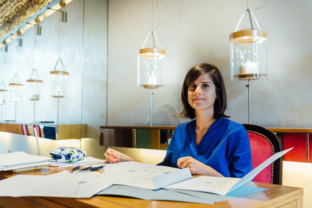 Jewellery designer Cynthia Raffoul sits at a desk in her boutique studio with design sketches and samples.