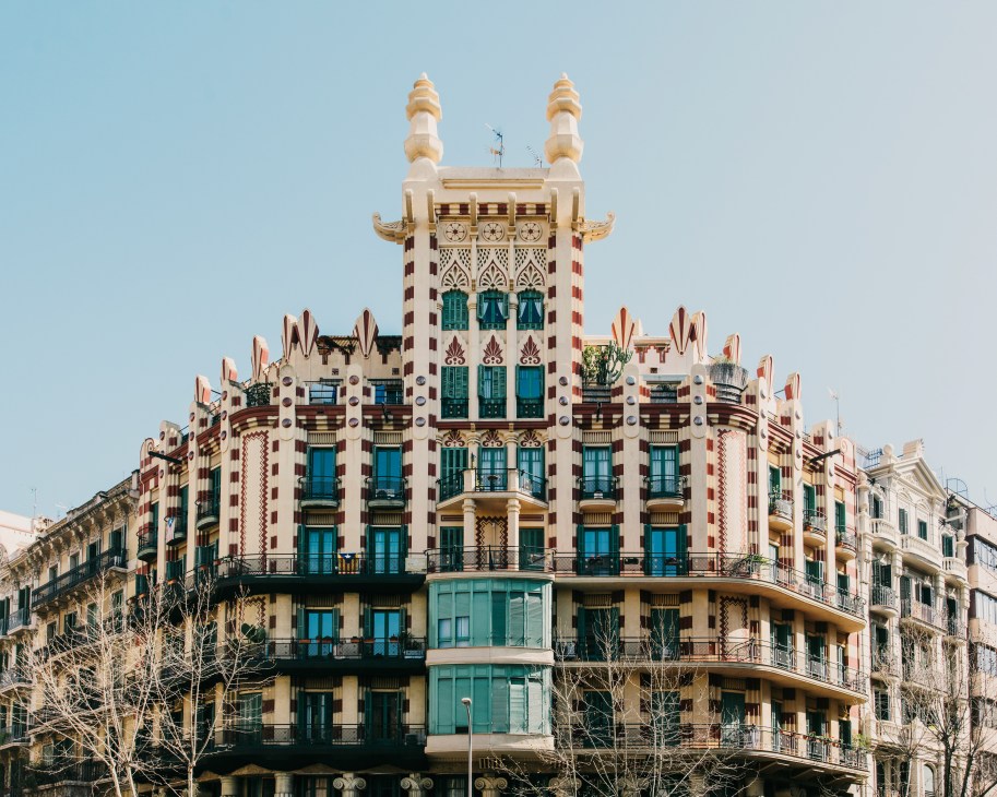 Casa Xina's ornate facade with pagoda-crowned turrets, Egyptian-inspired medallions, and teal window shutters in Barcelona's L'Eixample district.