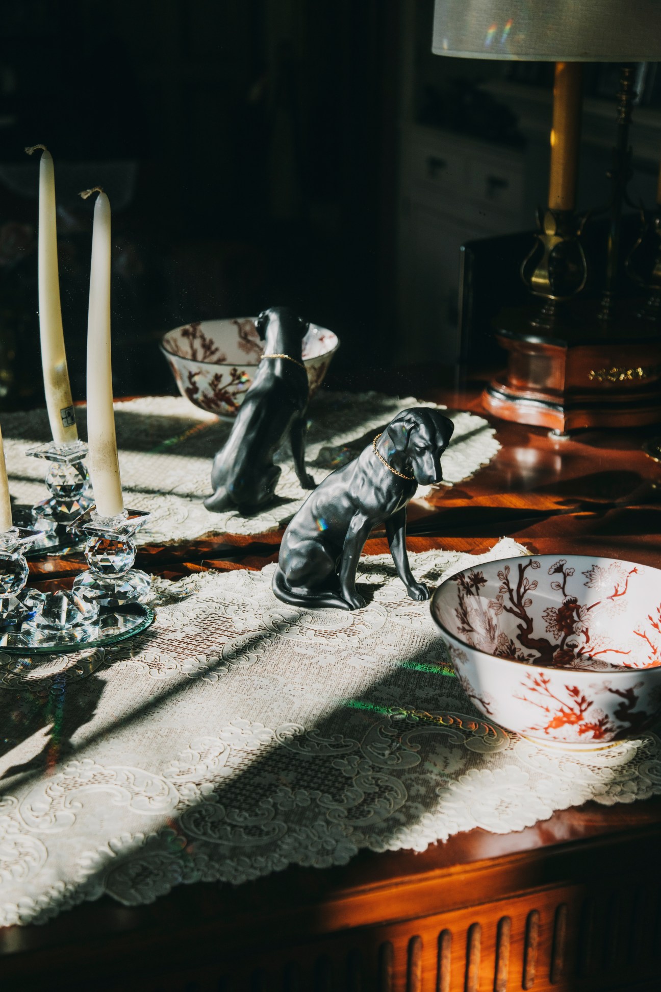 Decorative table arrangement with ceramic bowls, black dog figurines, candlesticks, and patterned textiles in evening sunlight.