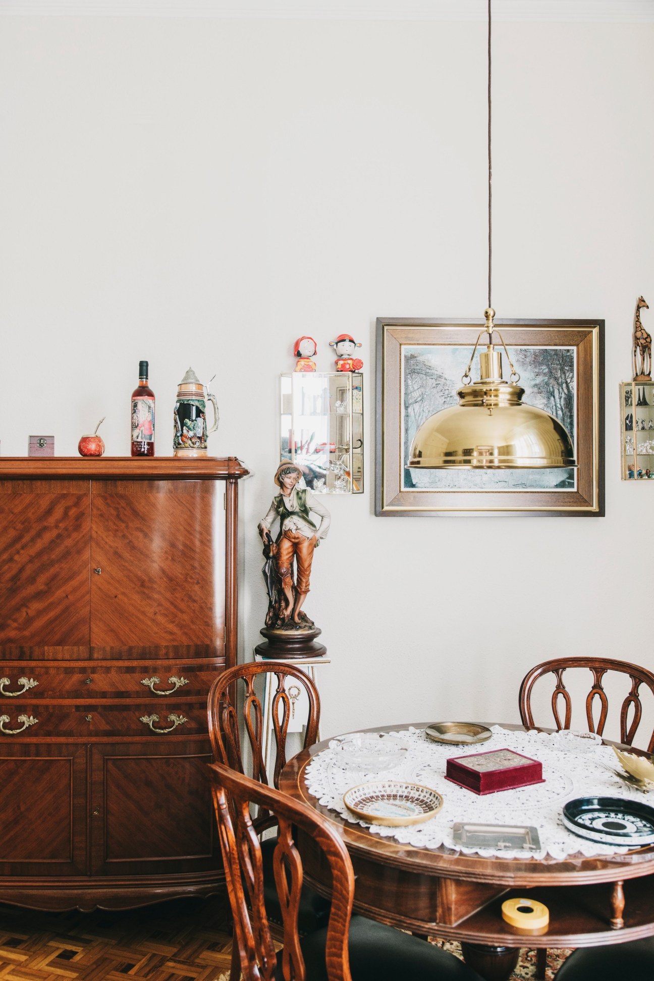 Vintage dining room with wooden furniture, decorative objects, and brass pendant lamp above round table.
