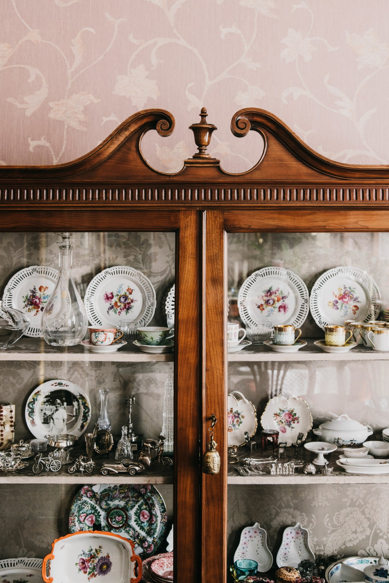 Wooden display cabinet with ornamental crest holding decorative plates and porcelain dishware.