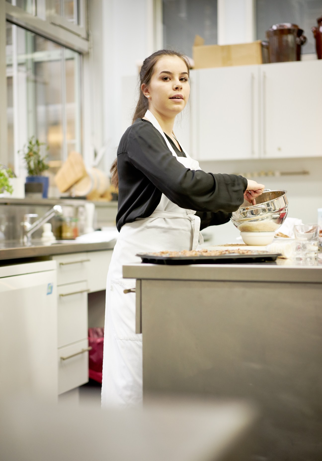 Chef in apron and black jacket working at kitchen counter with mixing bowl in test kitchen.