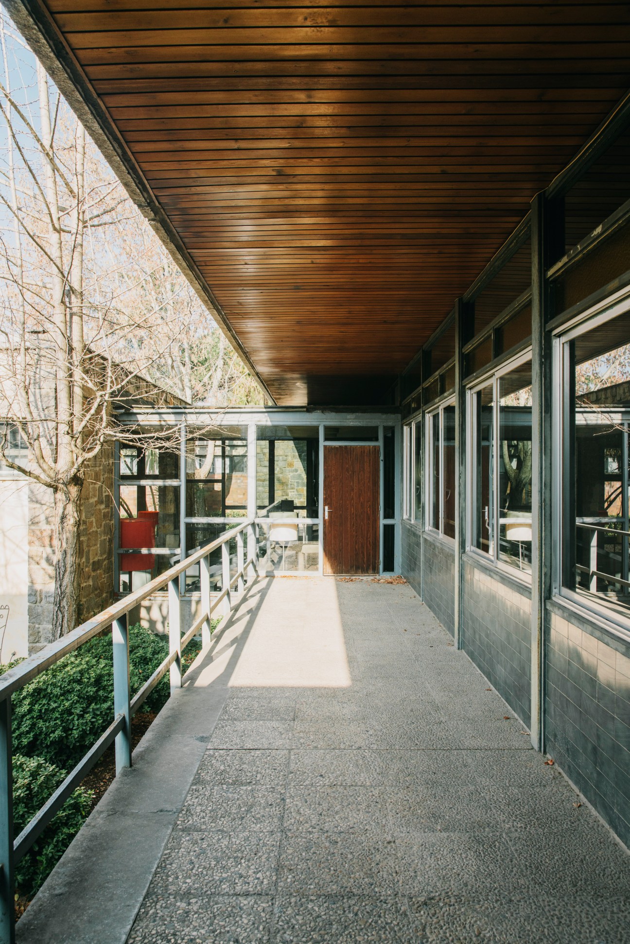 Covered exterior corridor with wooden ceiling, metal railings, and glass windows at Parc de Belloch.