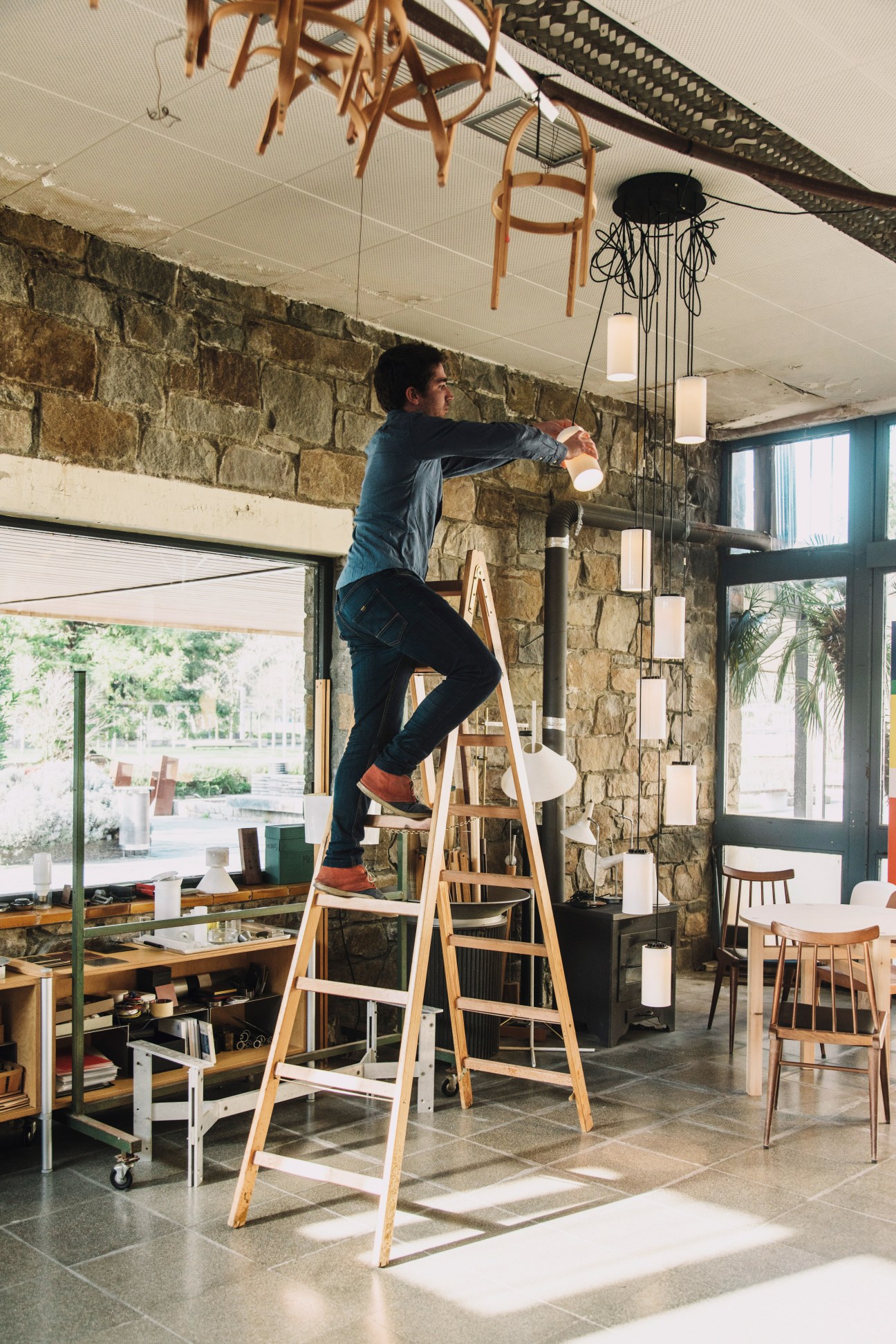 Man on ladder installing the Cirio Cascade pendant light fixture in a stone-walled interior space.