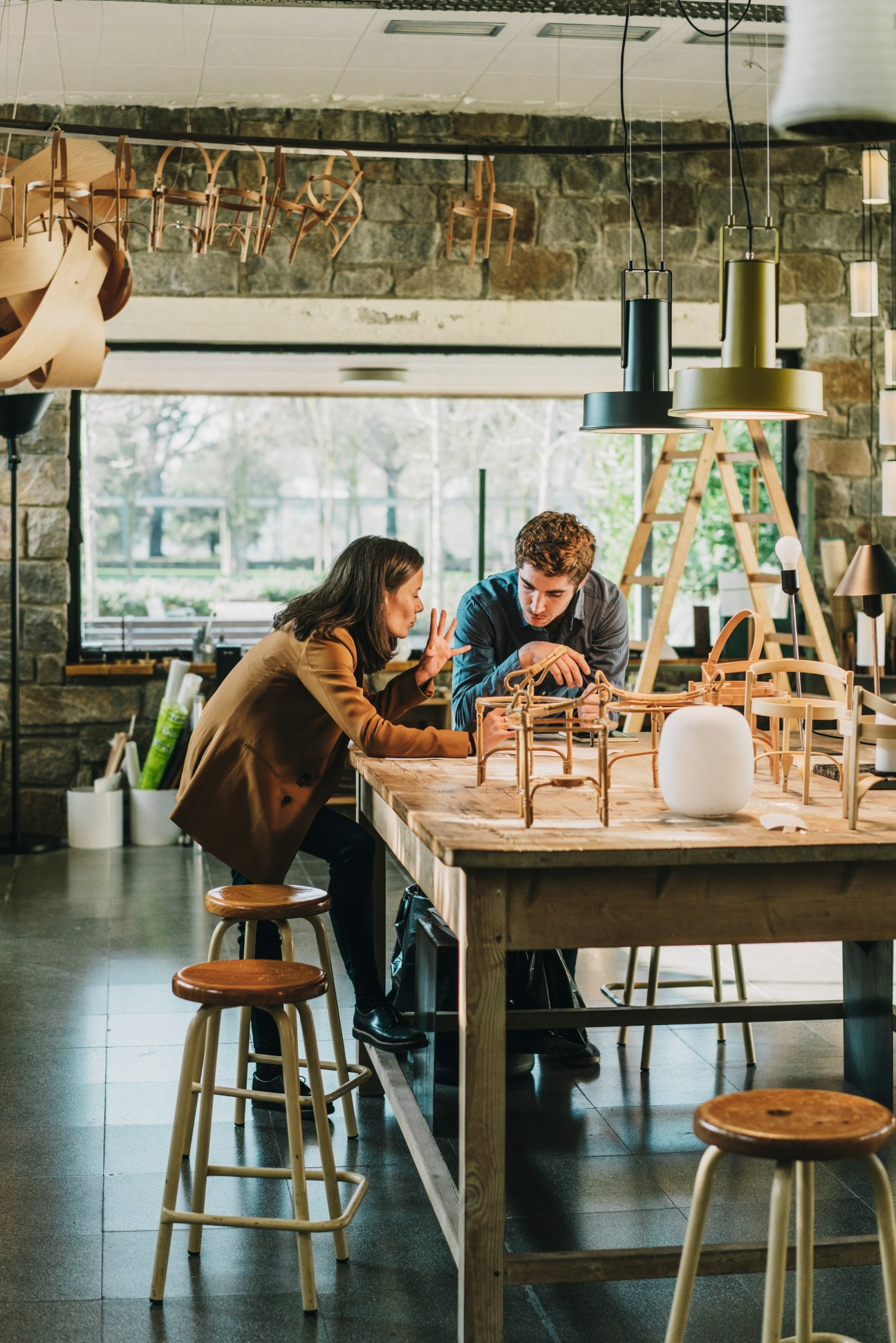 Editor Clàudia Roselló and technician Bernat Bisbal examining wooden chair prototypes at a workbench in the Santa & Cole studio.