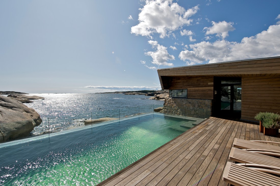Norwegian seafront summerhouse by JVA with wooden deck, infinity pool and rock formations overlooking the sea.