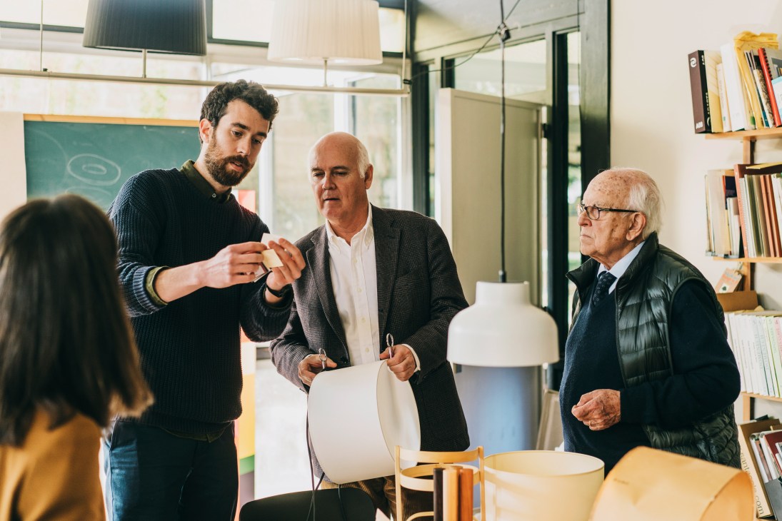 Designer Miguel Milá discussing lamp prototype with editor David Martí and executive VP José Maria Milá in workshop.