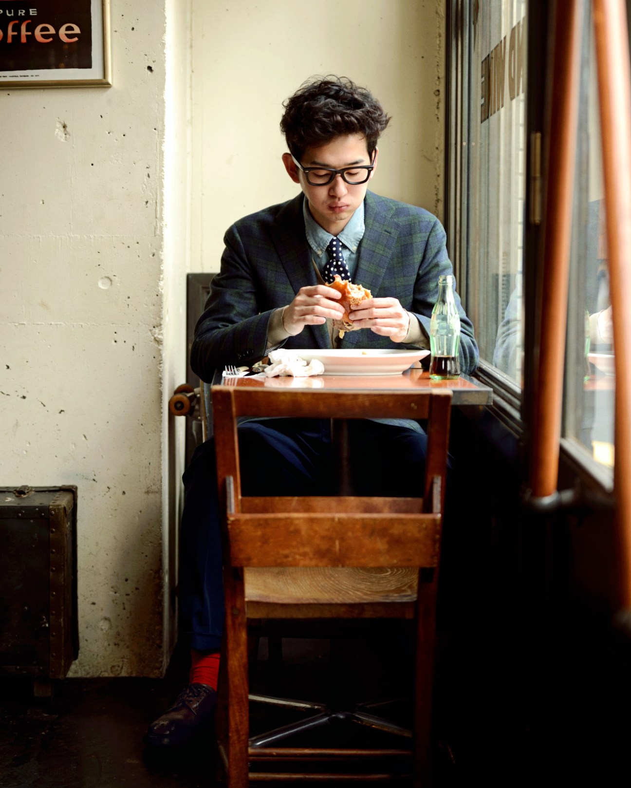 Man in blazer and tie eating a hamburger alone at a café table in Tokyo.