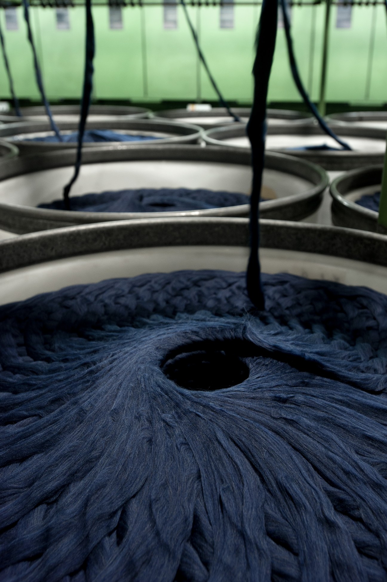 Dark blue merino wool fibers in processing vats with overhead equipment at a textile mill.